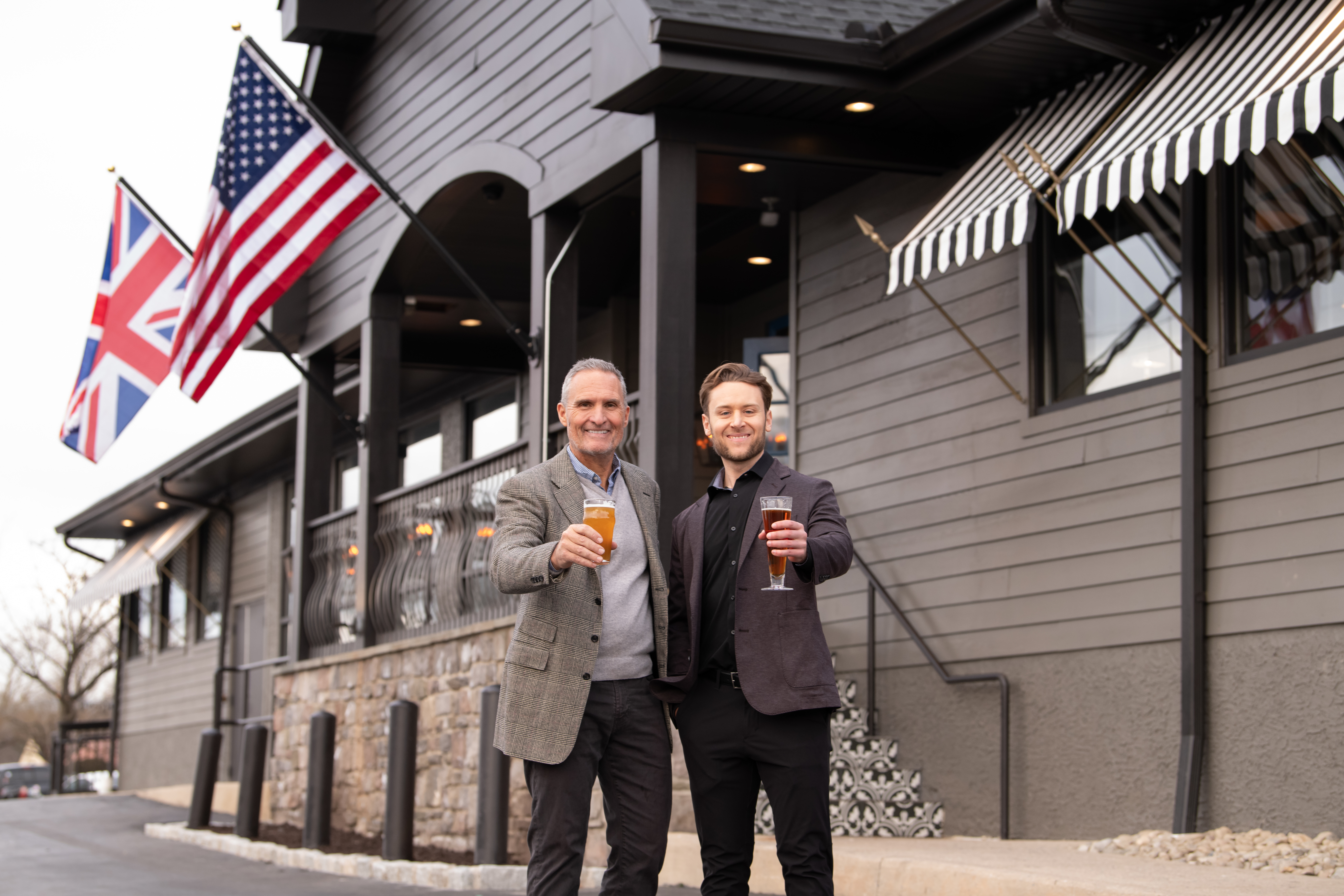 Father and son standing outside their restaurant raising a beer